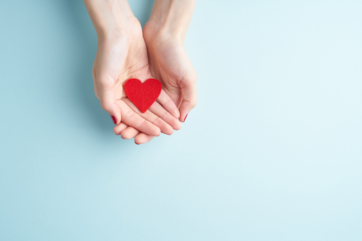 a person holding red heart in hands, donate and family insurance concept, on aquamarine background, copy space top view hemstädning