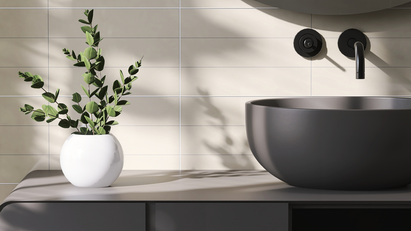 Modern and luxury dark gray bathroom vanity with counter top, round ceramic washbasin and black faucet in sunlight from window with vase of houseplant hemstädning